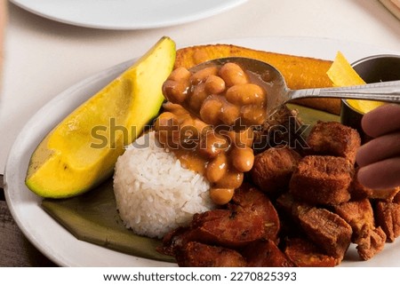 Person serving bean soup on the plate of additions of rice, avocado and fried pork, traditional Colombian lunch