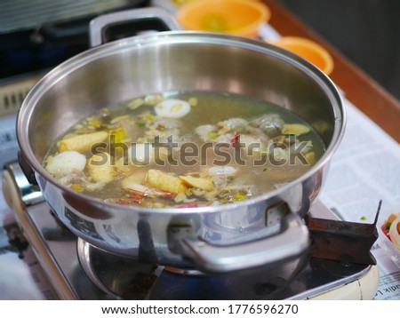 Person serving steaming hot Asian soup into a bowl at a home during a family meal - Asian family diner at a table holding spoon full of Thai Tom Yum spicy soup with summer filter