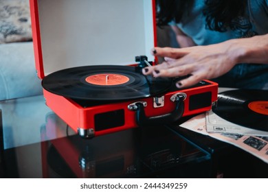 A person setting the tonearm on a vinyl record on a red portable turntable, preparing for music play