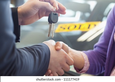 Person Shaking Hands In Front Of A Sold Car In A Car Shop