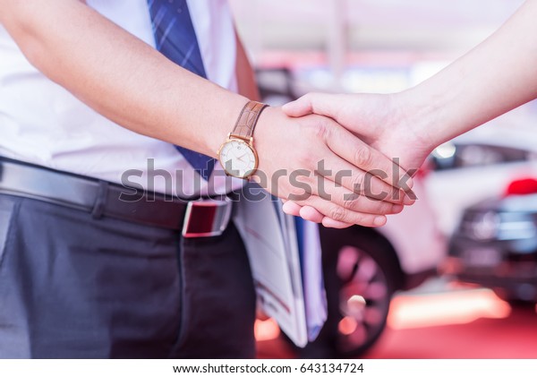 Person shaking hands in front of a sold car at\
new car showroom