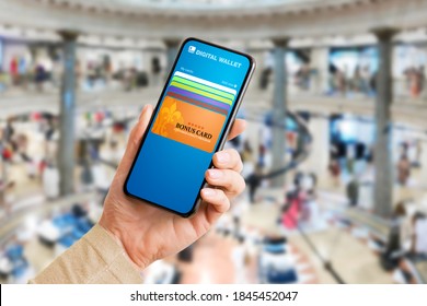 Person in shopping mall using mobile app on phone with bonus and customer loyalty program cards for discounts or special offers.