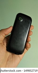 Person Showing The Back Side Or Back Cover With Camera Of A Old Feature Mobile Phone