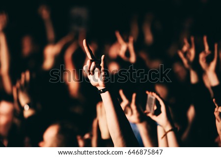 Person showing sign of the horns during a rock band concert in club.  A crowd of people at during a concert. Two finger rock hand.