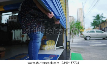 Person shutting storefront garage. Female entrepreneur closing local shop