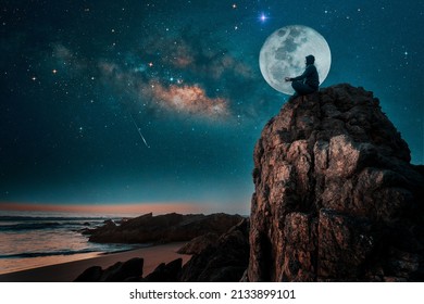 Person Silhouette Sitting On The Top Of The Mountain Meditating Or Contemplating The Starry Night With Milky Way And Moon Background	