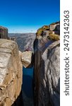 A person sits on the edge of Pulpit Rock in Norway, gazing out over the breathtaking landscape. The sheer drop-off and dramatic rock formations offer a stunning visual contrast to Kjergabolten Norway