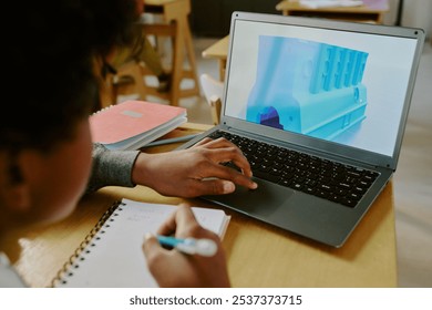 Person sitting in classroom while learning 3D modeling with laptop in front of them and notebook for jotting down notes. Focus on laptop screen showing 3D model