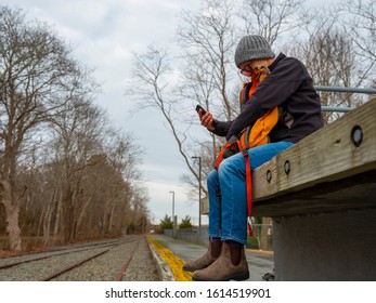 Person Sitting On Small Town Rail Platform Checking Their Mobile Phone