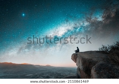 person sitting on the top of the mountain meditating or contemplating the starry night with Milky Way background	