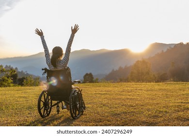 Person sitting on a wheelchair enjoying with raised hands on the mountain at the sunset time. - Powered by Shutterstock