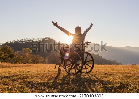 Person sitting on a wheelchair enjoying sundown on mountain background.