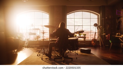 Person Sitting With Their Back To Camera And Playing Drums During A Band Rehearsal In A Loft Studio With Sunlight. Drummer Practising Alone Before A Concert On Stage. Warm Color Editing.