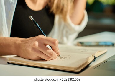 Person is sketching in notebook while working remotely at desk with laptop. Freelance work at home office. Graphic designer drawing sketch