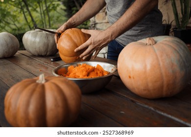 A person slices open a large pumpkin on a wooden table, surrounded by whole pumpkins and an orange pulp-filled bowl, highlighting autumnal preparation and harvest themes. - Powered by Shutterstock