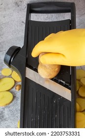 Person Slicing Potato On A Kitchen Mandolin Cutter. On A Concrete Background