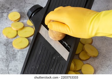 Person Slicing Potato On A Kitchen Mandolin Cutter. On A Concrete Background