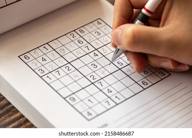 A person solving a sudoku puzzle on a wooden table