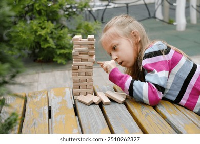 Person stacking wooden blocks, building tower while seated at a table outdoors, concentrating on balancing the pieces. Closeup - Powered by Shutterstock