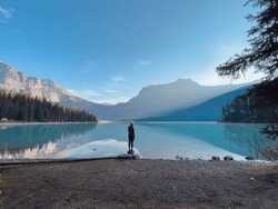 Person Standing Alone On Rock On Lake In Early Morning Sun Rays Canadian Rockies