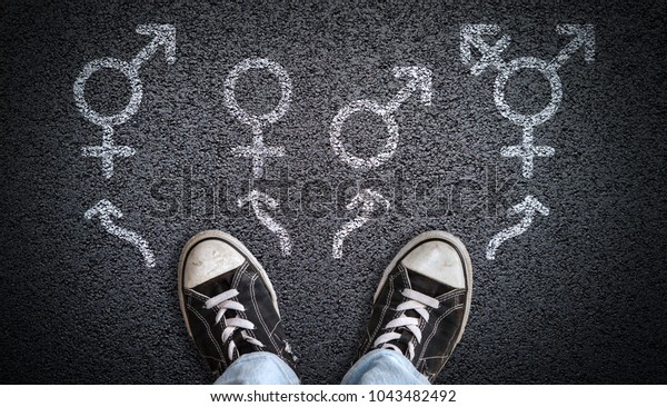 A person standing on asphalt road\
with gender symbols of male, female, bigender and transgender. \
Concept of choice or gender confusion or\
dysphoria.