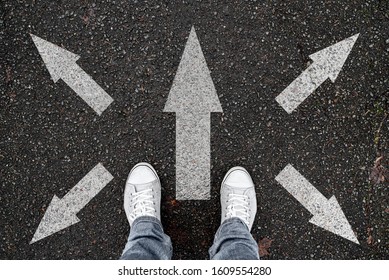 Person Standing On Road With Arrow Markings Pointing In Different Directions, Decision Making Concept