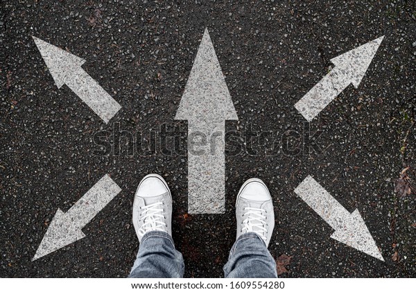 person standing on\
road with arrow markings pointing in different directions, decision\
making concept