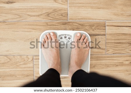 Person standing on scale measuring weight on wooden floor. Health and fitness concept focusing on weight management and wellness.