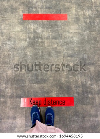 Person standing on tiled floor against a red line with the words 'keep your distance'. Concept of keep distance, social distancing, quarantine or isolation