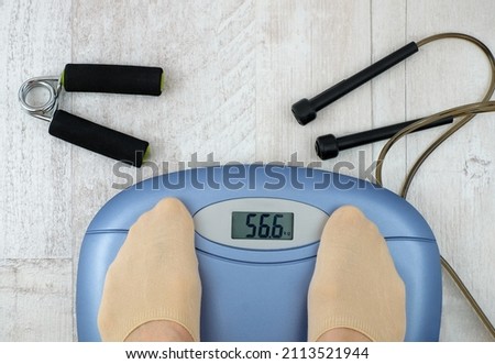 Person standing on a weight scale. Feet on weight scale and fitness accessories on wooden floor