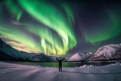 Person Standing In A Snowy Landscape With The Northern Lights In The Sky