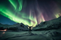 Person Standing In A Snowy Landscape With The Northern Lights In The Sky