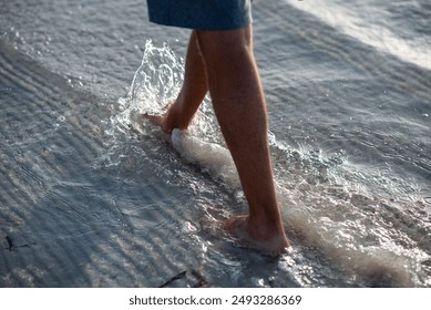 A person stands barefoot on the beach, feet splashing in water, surrounded by wooden planks. Keywords Water, Shoe, Leg, Cloud, People in nature, People on beach, Thigh, Barefoot, Wood, Beach - Powered by Shutterstock