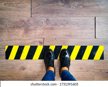 Person Stands In Line With Yellow And Black Stripes Keeping Safe Social Distance Due To A Pandemic. Legs Of A Girl In Jeans Waiting In Line At Checkout Counter In Supermarket Top View


