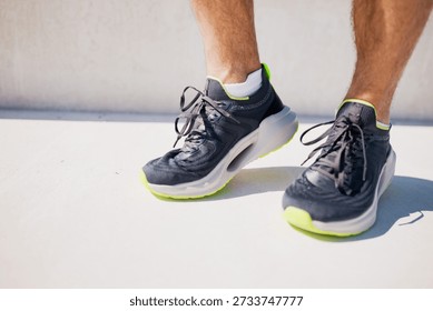 Person stands on a solid surface wearing black and green running shoes in bright daylight on a sunny day