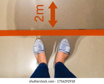 Person Stands In Red Line Keeping 2m Safe Social Distance Due To Pandemic Legs Of Girl In Jeans Waiting In Line At Checkout Counter In Supermarket Top View