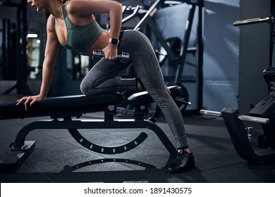 Person Steadying Herself Against The Bench With One Hand While Lifting A Hand Weight With The Other