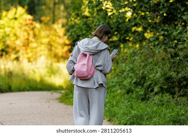 A person strolls down a winding path, absorbed in their phone amidst the vibrant greenery of nature.