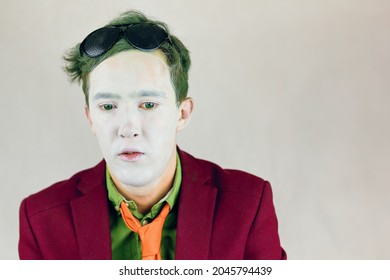 Person In Suit With Yellow Stripes Tie Looks Down. Actor With White Makeup On Face And Green Eyes And Hair. Paint Of Clown Or Mime. Theater Concept. Black Glasses On Head.