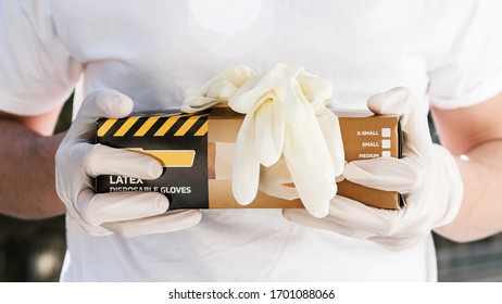 Person With Surgical Gloves Holding A Box Of Disposable Latex Gloves. Covid-19 Pandemic.