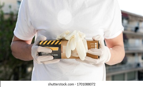 Person With Surgical Gloves Holding A Box Of Disposable Latex Gloves. Covid-19 Pandemic.