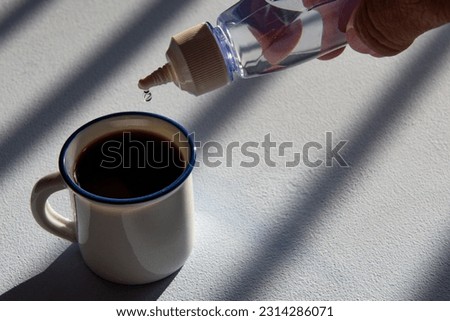 person sweetening coffee with liquid sweetener, scene showing cup and flask