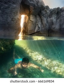 A Person Swimming Underwater, Behind Hole Rock, Half Underwater Shot.