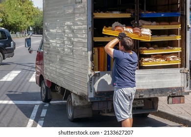 A person takes out a tray with bread from a machine designed to transport bakery products. The car is on the roadway, shelves with bread are visible inside.