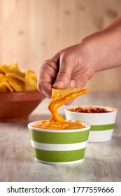 A Person Takes With Tortilla Chips Some Cheddar Cheese Dip, Vertically.