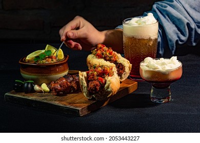 person taking a spoonful of pebre from the bowl to put it on his choripan, accompanied by a large terremoto glass, traditional food for national holidays in chile