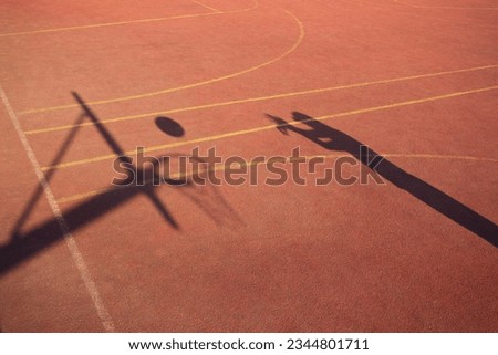 A person throwing a basketball to a hoop on an orange basketball court, shadow of person, basketball and net
