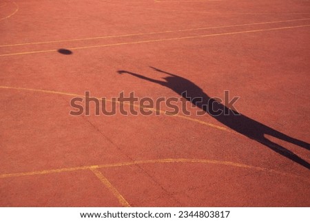 A person throwing a basketball on an orange basketball court, shadow of person and basketball in the air