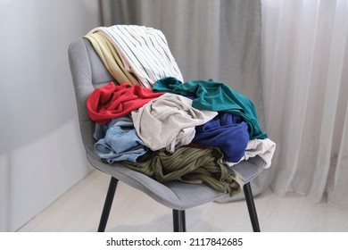 person throws used clothes on the chair. Pile clothes on chair. Heap of used clothes for donation and recycling.