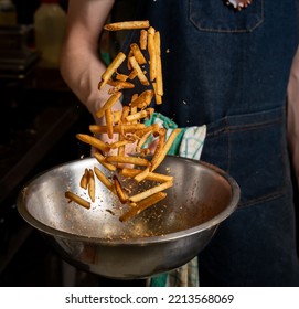 A Person Tossing Freshly Cooked Fries With Spices On A Mixing Bowl